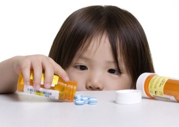 A young girl looks at a pile of pills that was left on a counter.; Shutterstock ID 5560465; Purchase Order: -